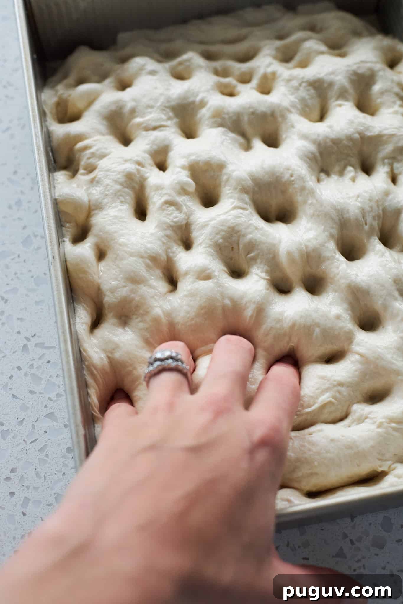 Sourdough Discard Cinnamon Roll Focaccia Recipe 9 A hand poking dimples in the dough.