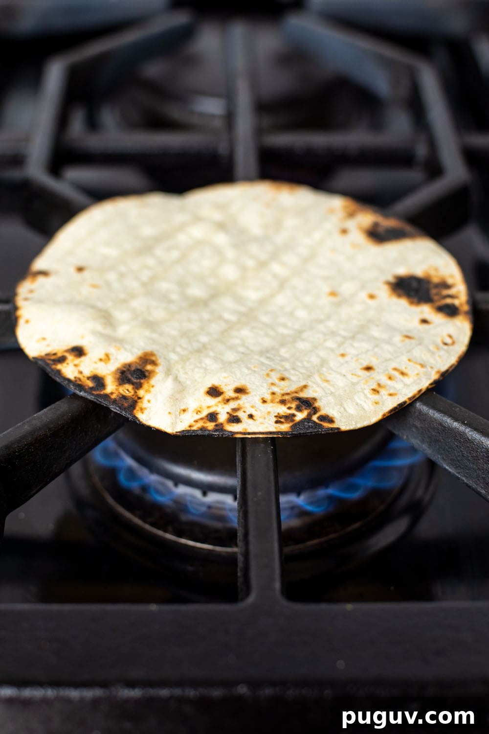 Toasting a corn tortilla on gas range until charred and crispy around the edges.