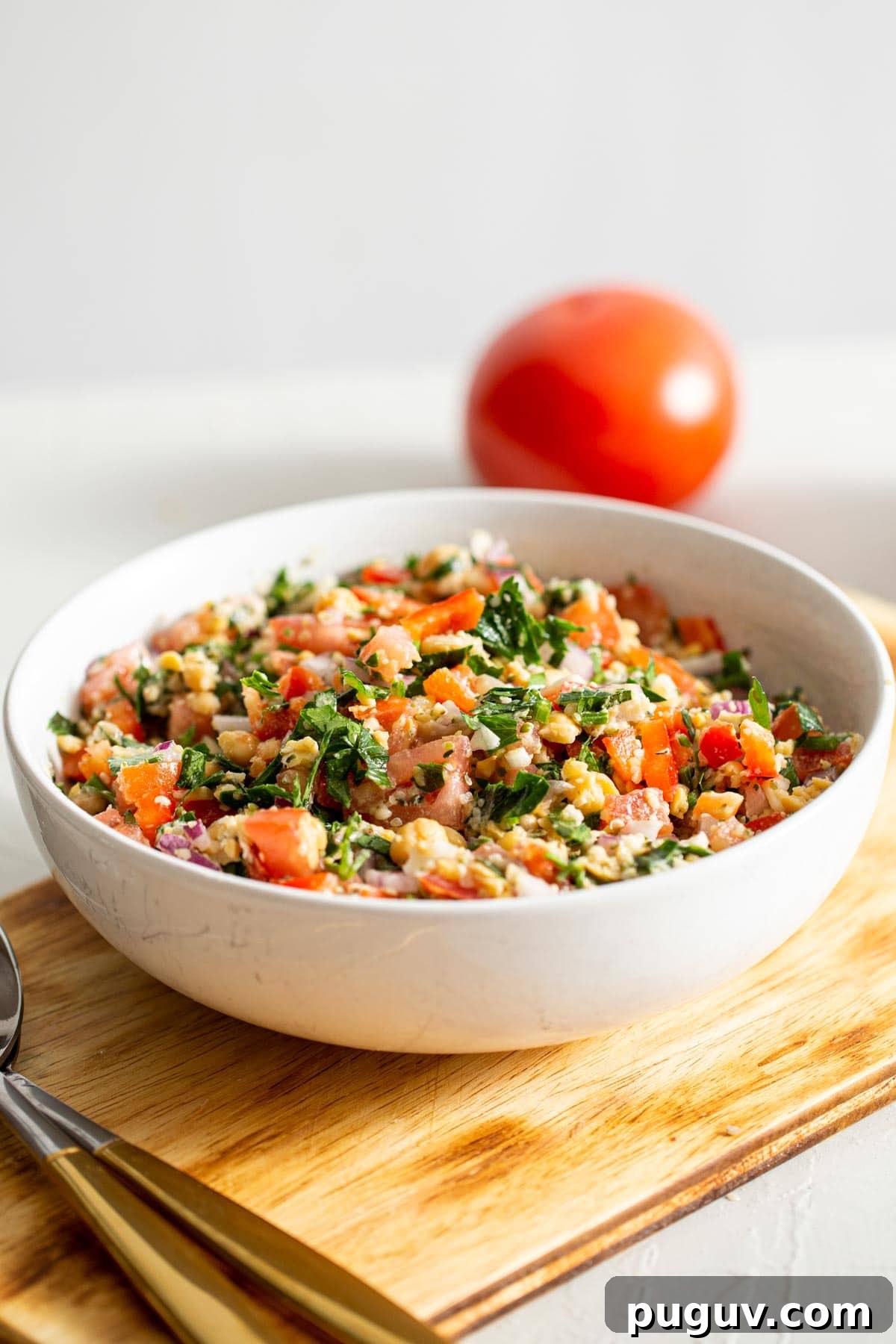 Chickpea Tabbouleh Salad with Fresh Herbs and Lemon Dressing 2 A bowl of tabouleh salad with a tomato in the background.