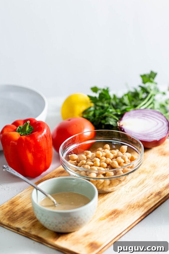 Chickpea Tabbouleh Salad with Fresh Herbs and Lemon Dressing 3 Chickpeas, tahini, bell pepper, onion, parsley and red onion on a cutting board.