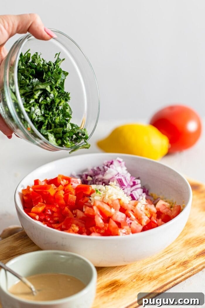 Chickpea Tabbouleh Salad with Fresh Herbs and Lemon Dressing 5 A bowl of chopped parsley being added to a bowl of fresh chopped veggies.