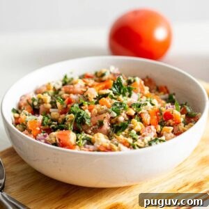 Tabouleh salad in a bowl with a tomato in the background.