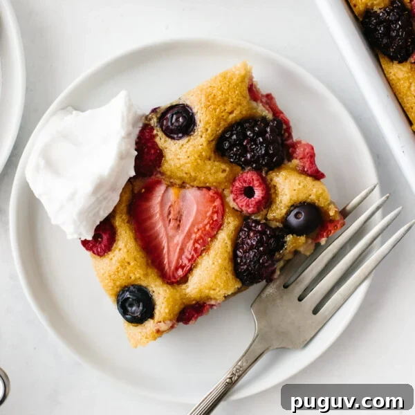 A slice of berry sheet cake on a white plate with fork and dollop of cream.