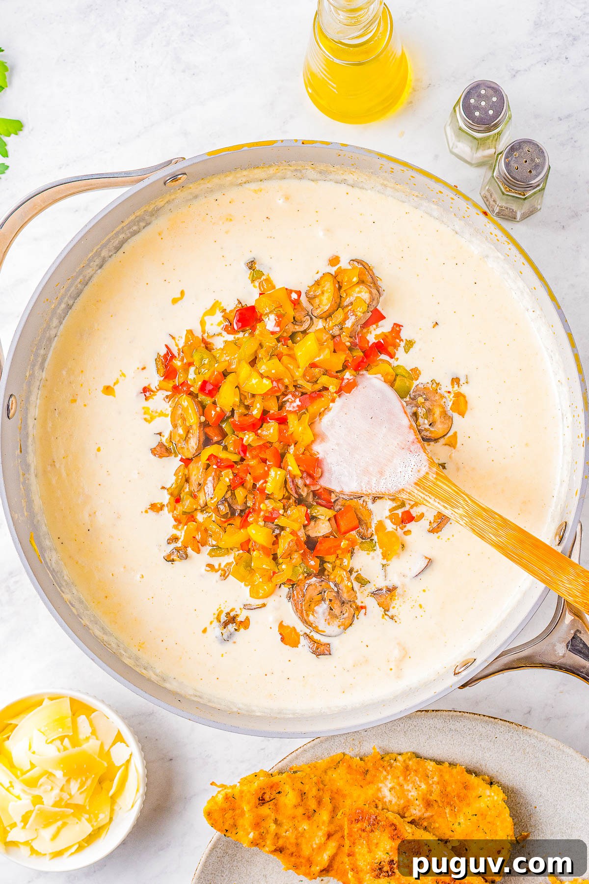 Sautéed vegetables being stirred into a cream sauce.