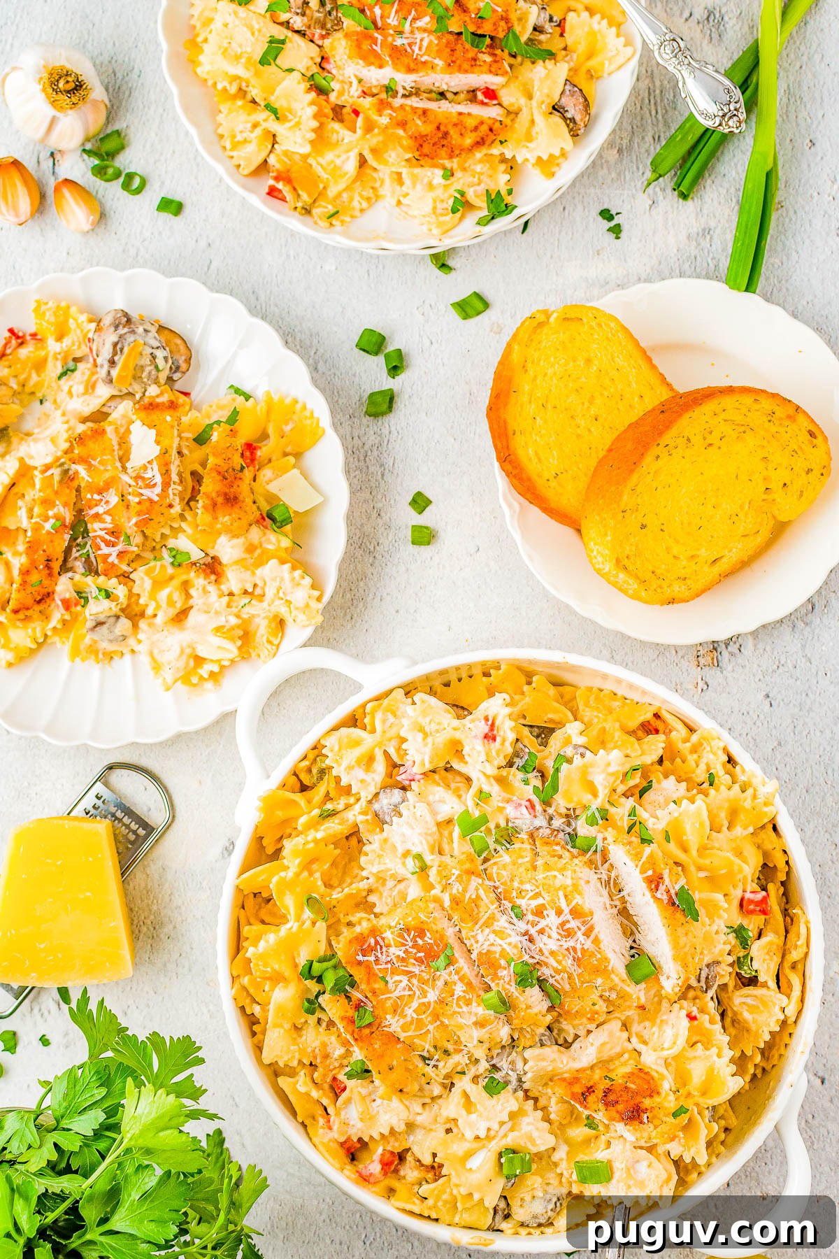 A bowl of Cajun chicken pasta, a plate of the pasta, and a plate with garlic bread pieces.