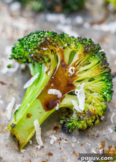 Roasted broccoli floret with melted cheese on a baking sheet.