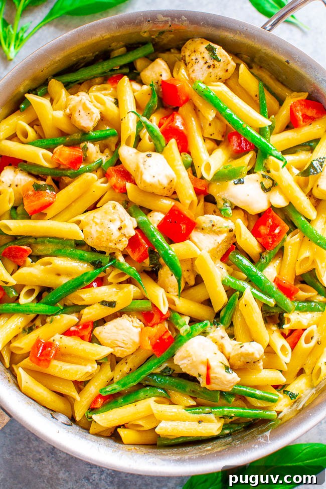 A colorful skillet of penne pasta mixed with vegetables and chicken pieces.