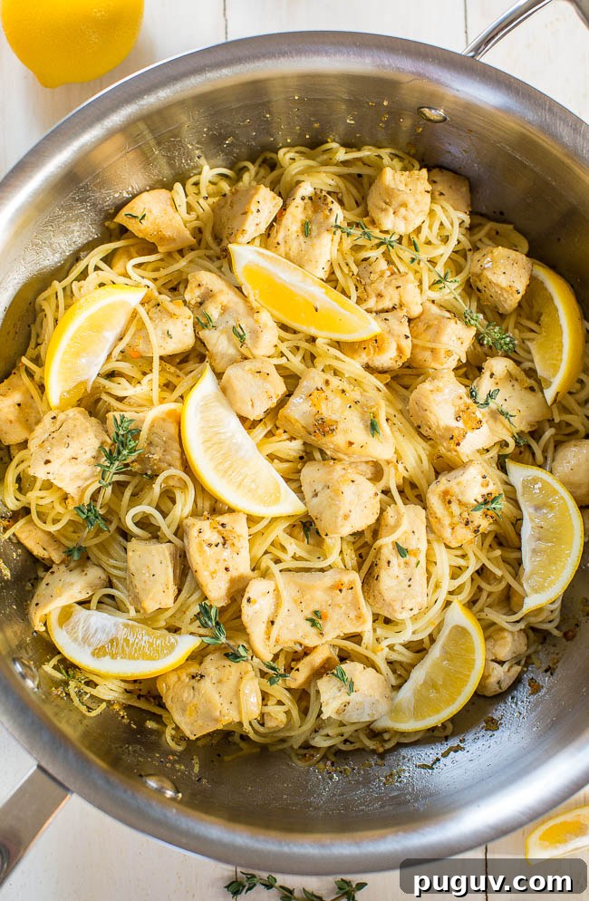 A skillet containing lemon chicken pasta garnished with fresh lemon slices and herbs.
