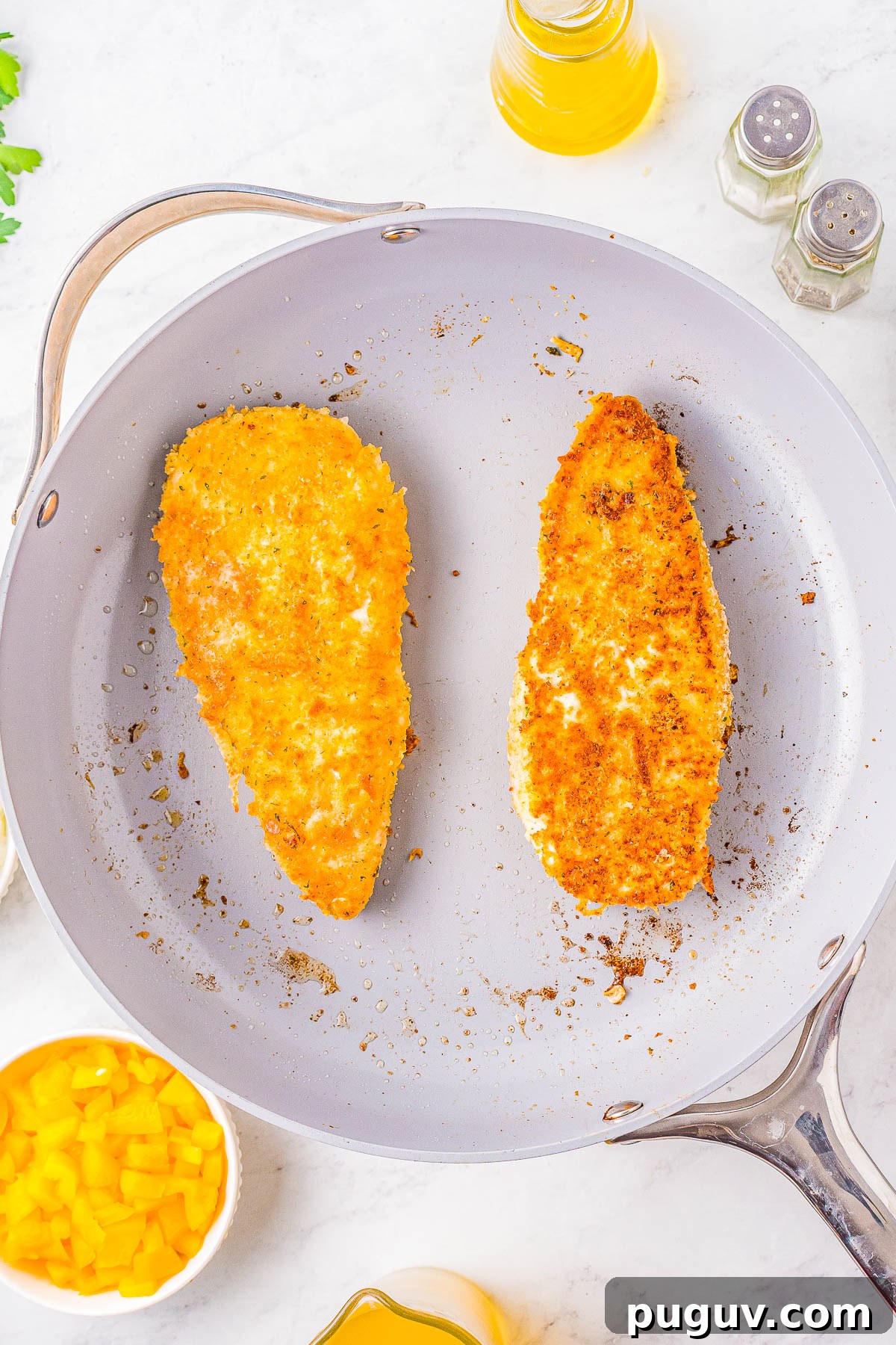 Two breaded chicken breasts in a skillet.