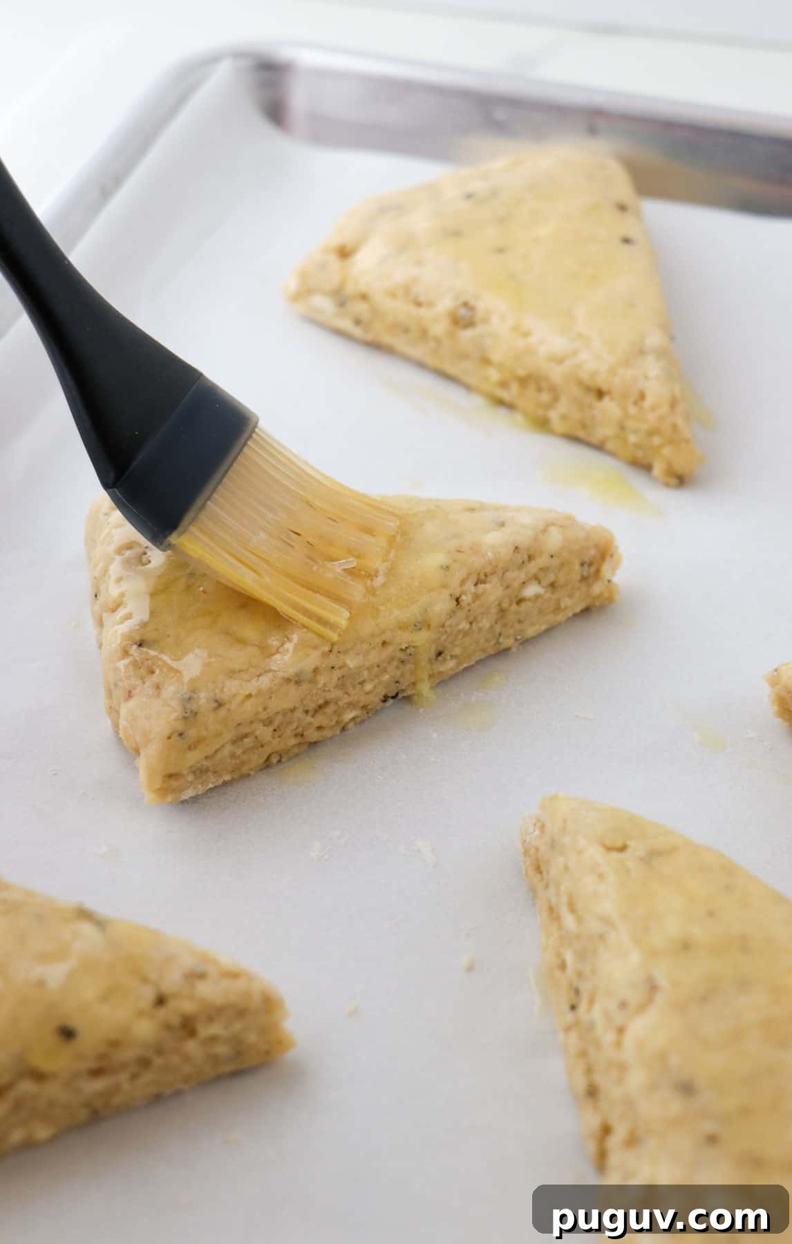 Brown Sugar Cardamom Scones Recipe for Tender, Buttery Pastries 9 Person brushing unbaked scones with melted butter.