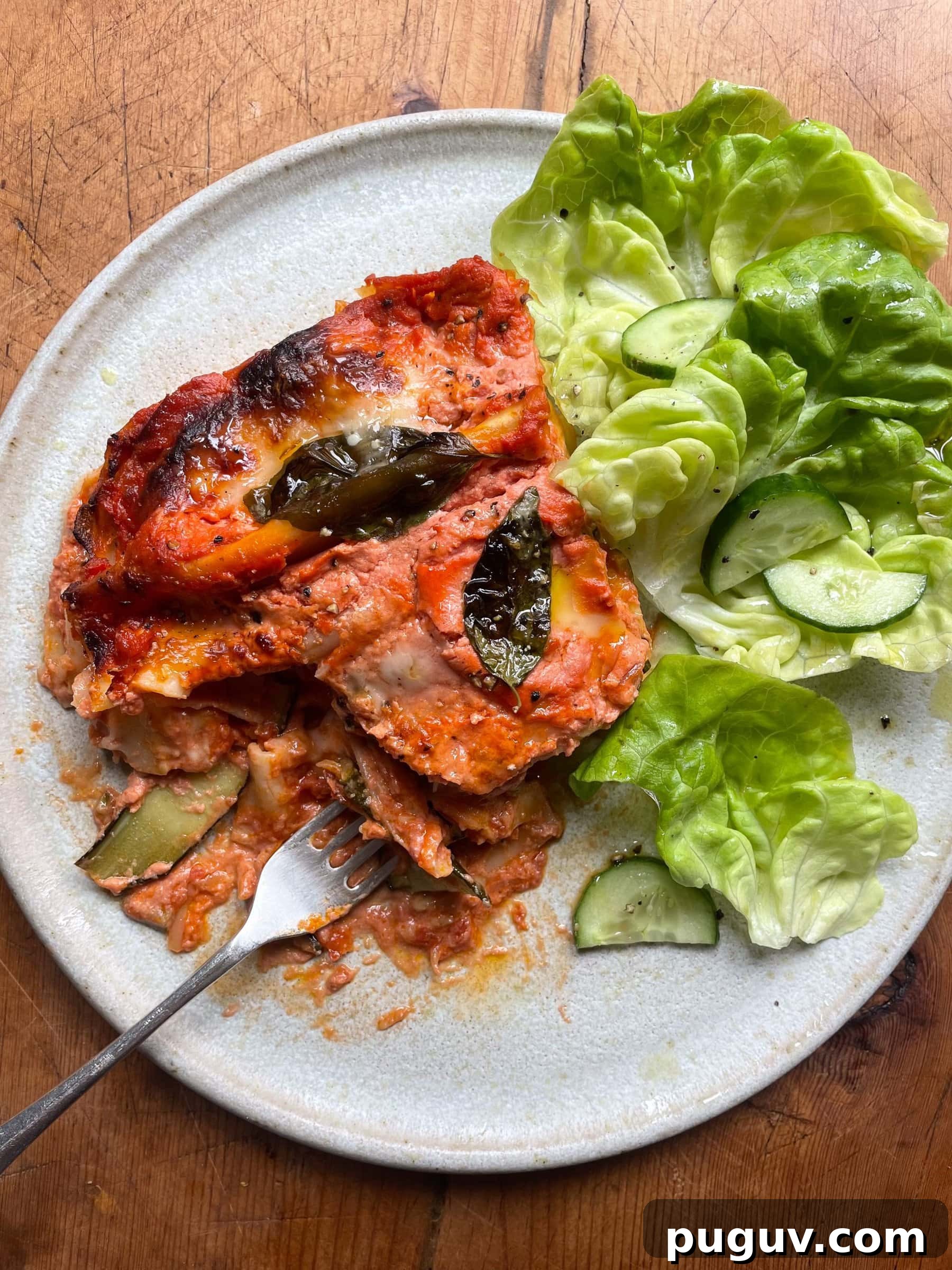 Piece of courgette lasagna on a white plate with a lettuce and cucumber salad.