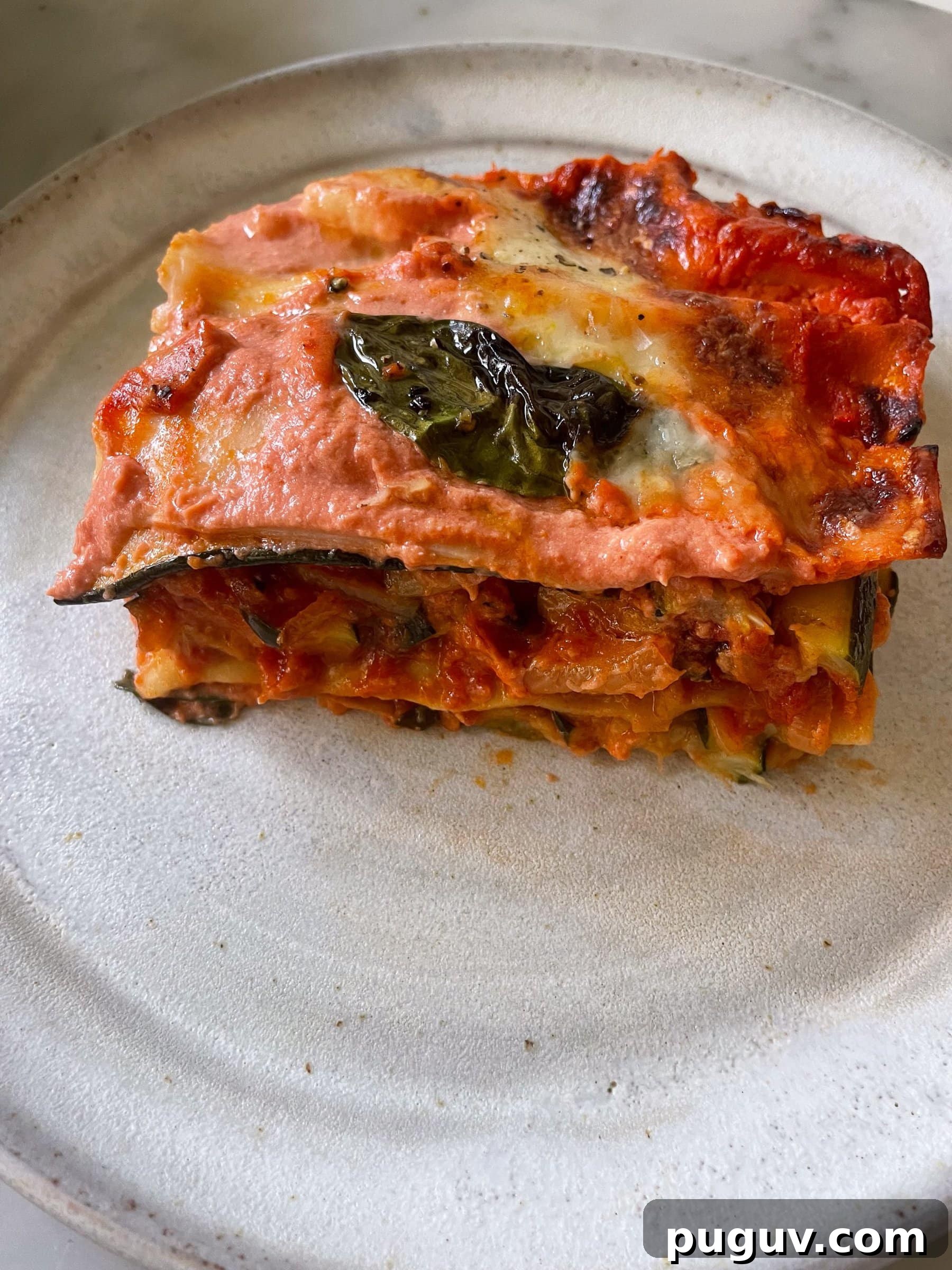 Side on view of a piece of zucchini lasagna on a white plate.