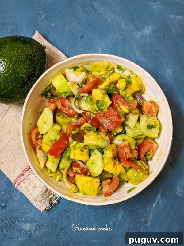 large avocado cucumber and tomato salad with onion slices in a white bowl with a blue background.