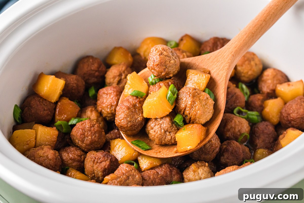 A wooden spoon holding a scoop of pineapple meatballs over a crockpot.
