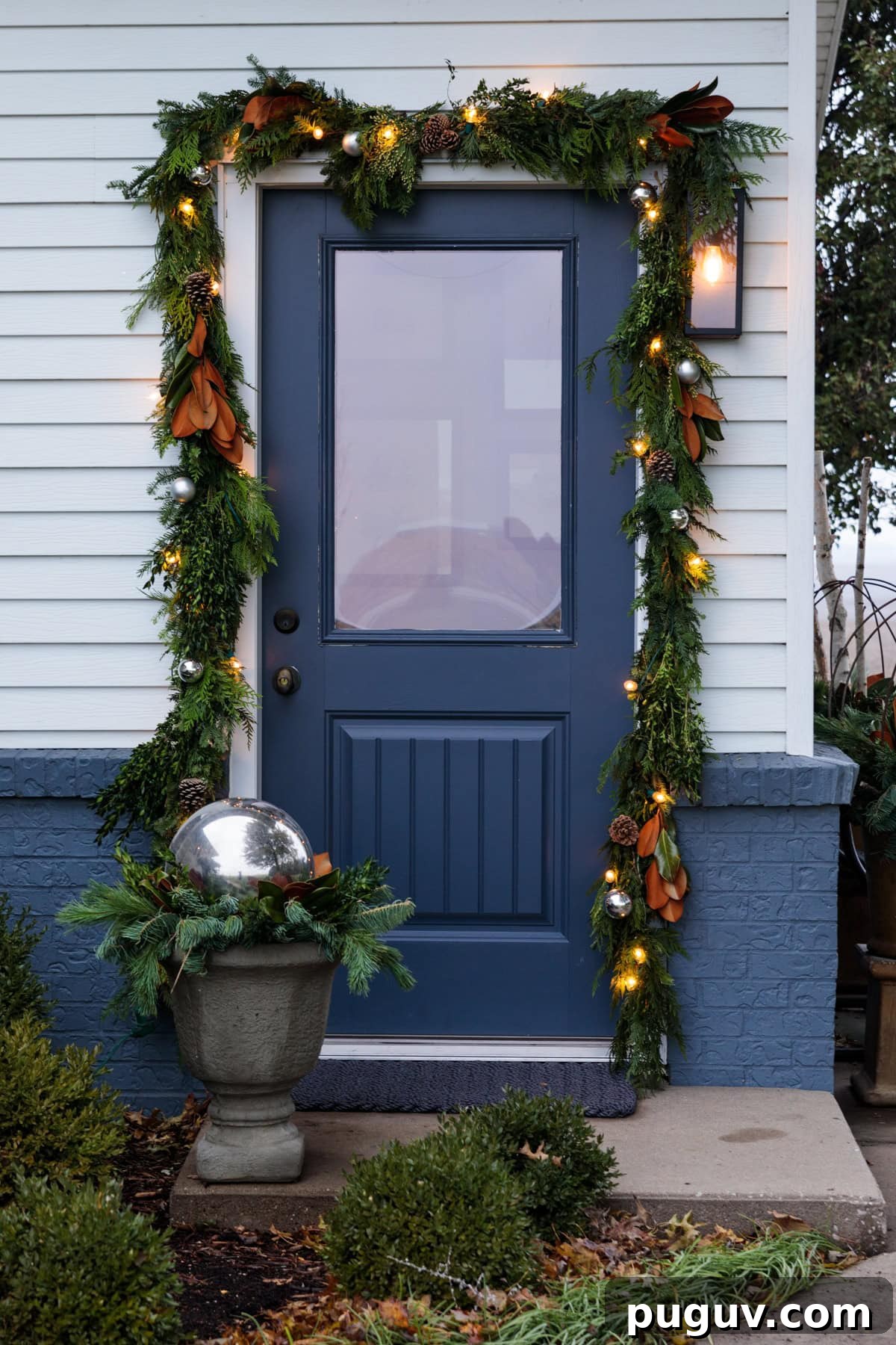 A blue front door adorned with garland all around with magnolia leaves and lights worked in as well.