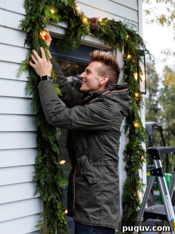 Kaleb Wyse wearing coat hanging Christmas garland with magnolia leaves and lights intertwined around doorway.