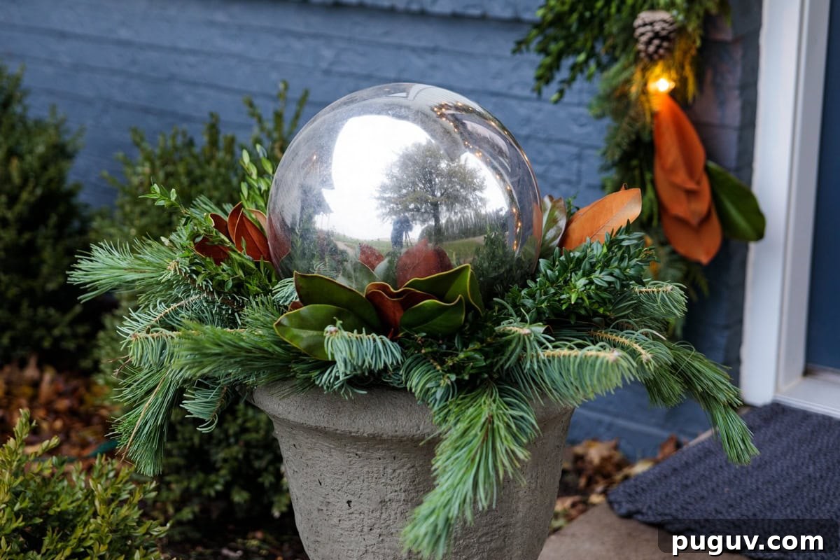 Silver gazing ball perched on top of greens and magnolia leaves in an urn for Christmas holiday decor.
