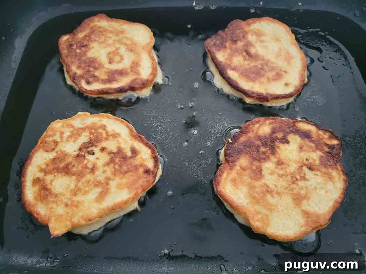 4 golden brown banana pancakes cooking in a skillet.