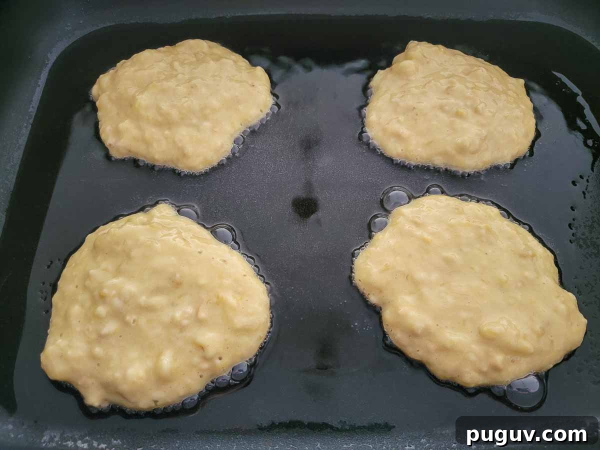 4 banana pancakes cooking in a skillet.