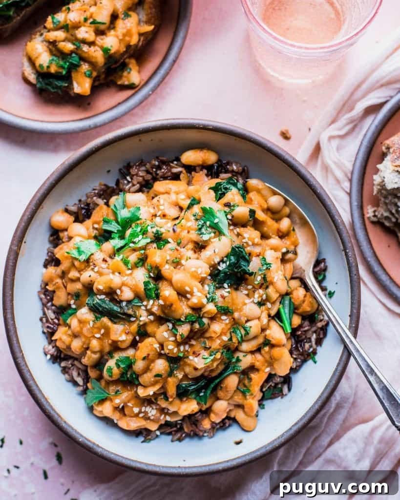 ceramic bowl on pink backdrop with creamy white beans and kale served over wild rice