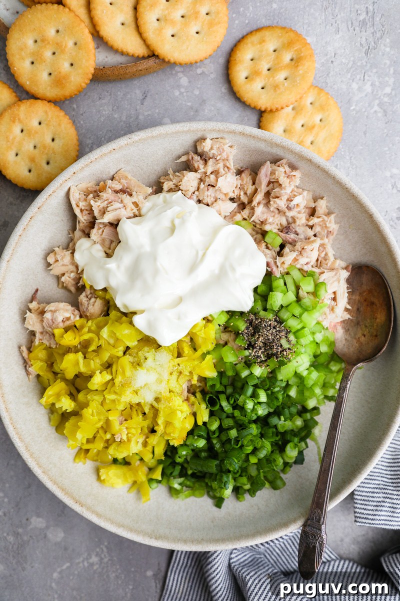 A large shallow bowl filled with canned tuna, celery, green onion, chopped pepperoncini, mayo, salt and black pepper