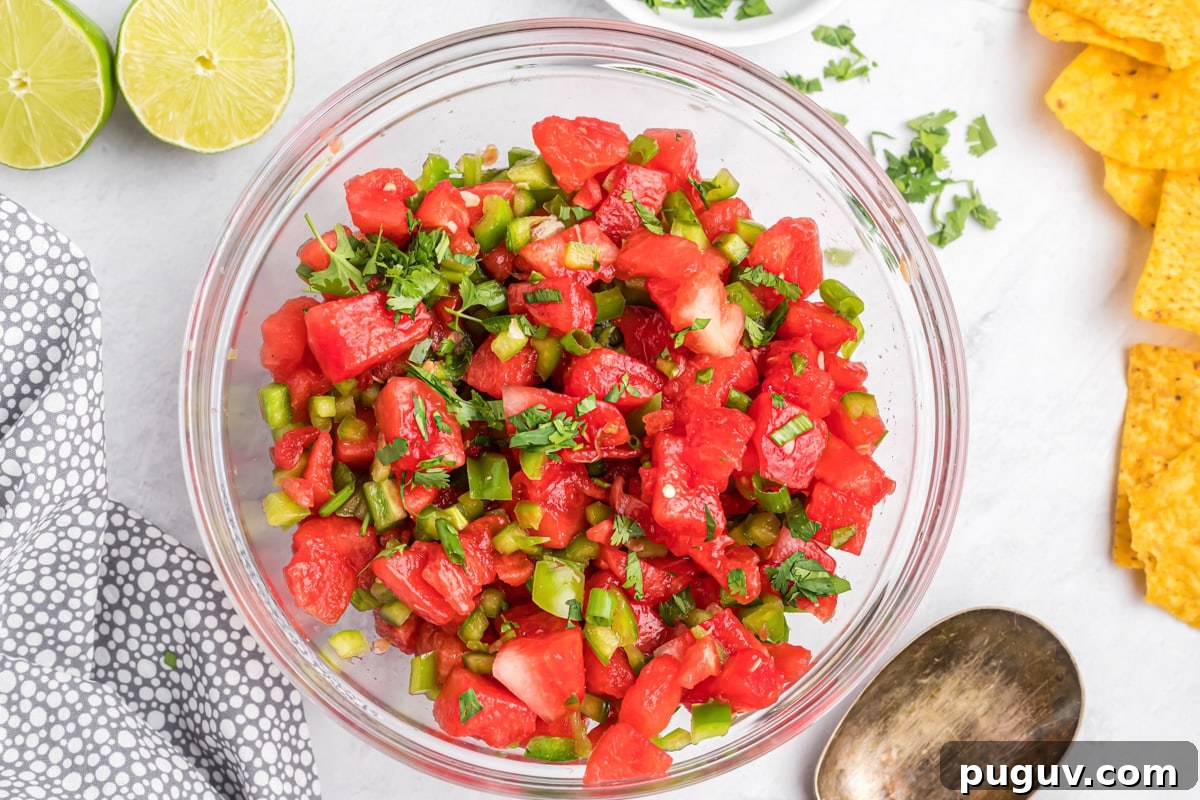 A bowl of fresh salsa with a fresh lime cut in half and tortilla chips beside it. 