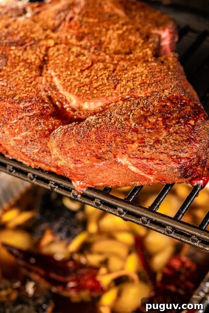 Seasoned chuck roast on grill grates above a pot of braise.