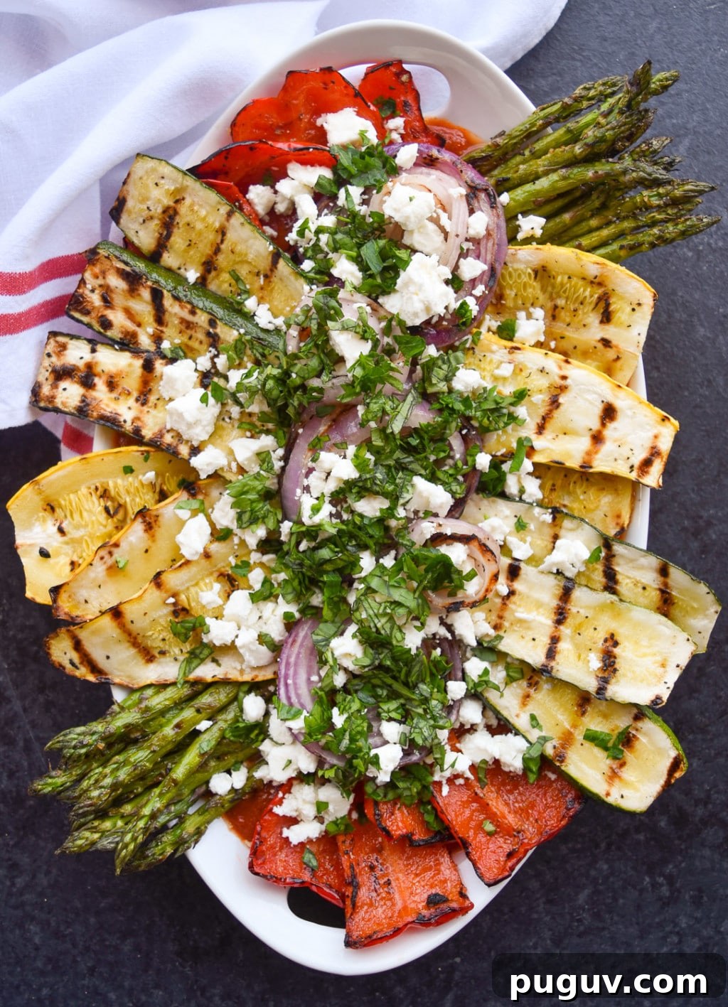 Close up of platter of grilled zucchini, yellow squash, onions, bell pepper, and asparagus topped with feta cheese and chopped herbs.