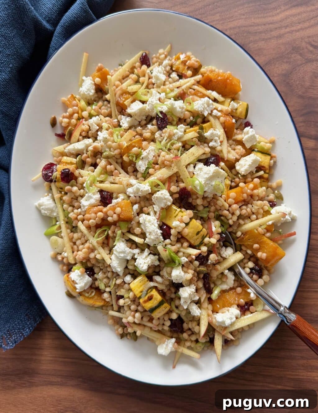 Overhead shot of fall couscous salad on a platter with a serving spoon and napkin.