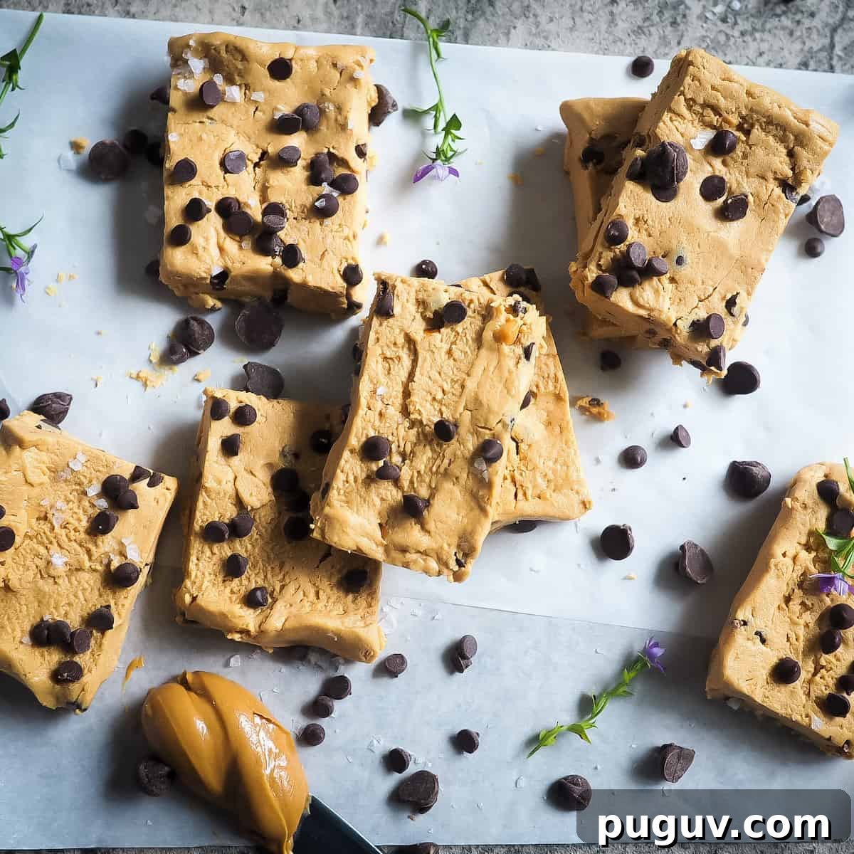 Peanut butter and chocolate chip perfect bars on a piece of parchment paper with a knife and a glob of peanut butter.