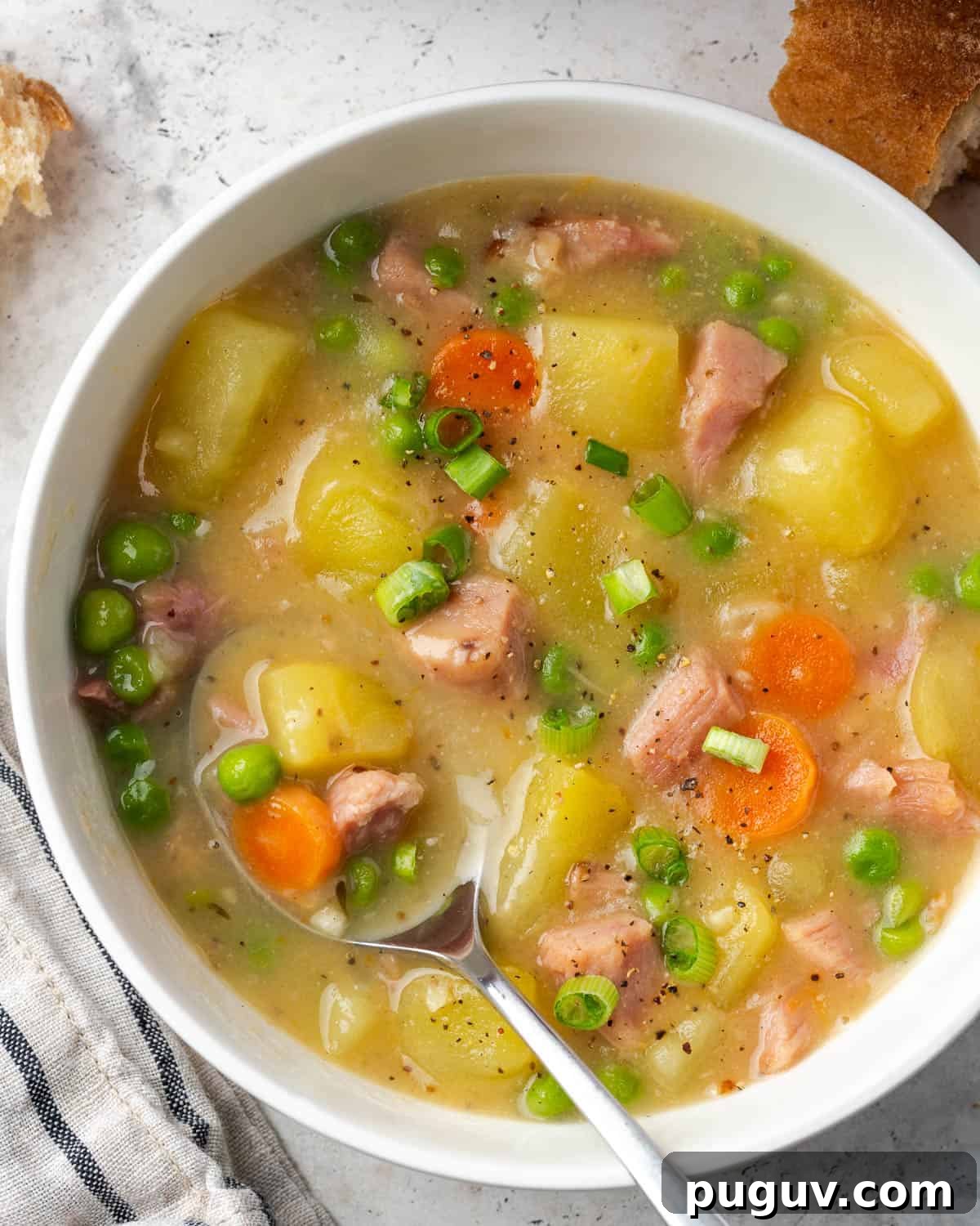 A spoon scooping up a bite of ham and potato soup from a serving bowl.