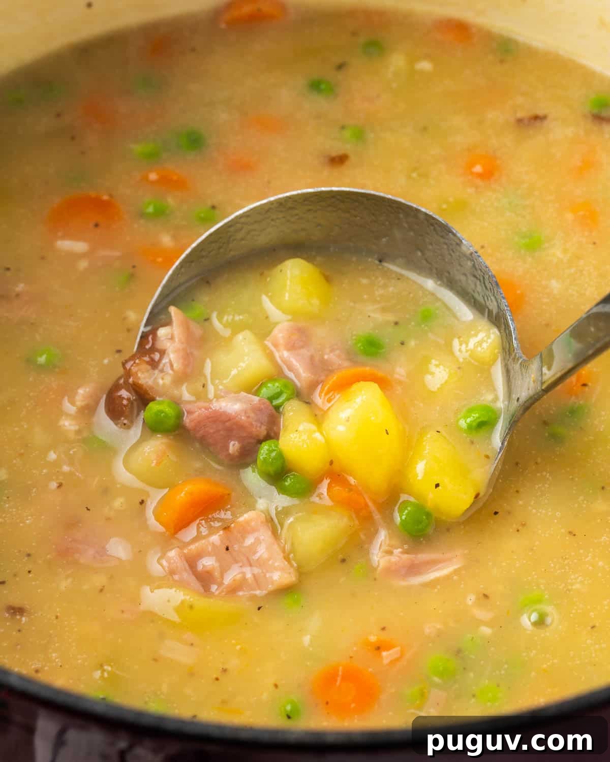 A ladle scooping up a serving of ham and potato soup from the pot.