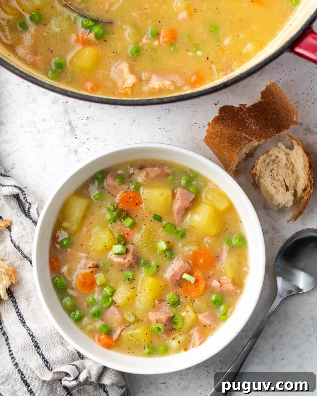 A bowl of ham and potato soup topped with green onions and served with gluten free french bread.