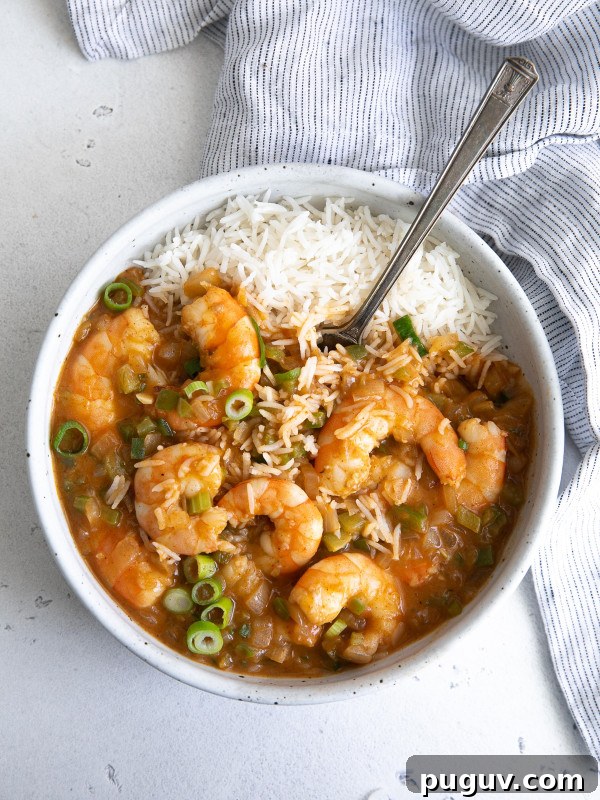 White serving bowl filled with cooked shrimp etouffee with a serving of cooked white rice.