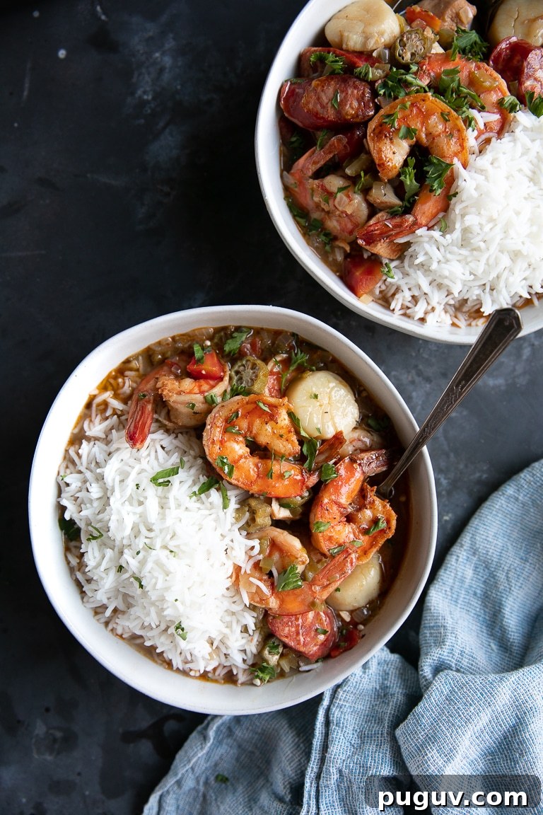 Two white bowls filled with seafood gumbo and white rice on a dark table.