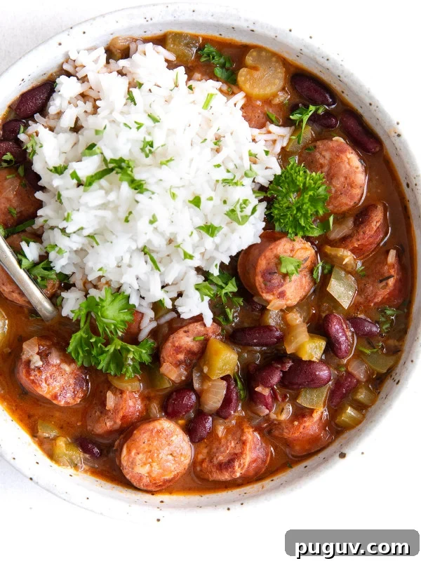 A hearty bowl of red beans stewed with smoked sausage, bell peppers, and onions, served alongside a generous scoop of fluffy white rice and garnished with parsley.