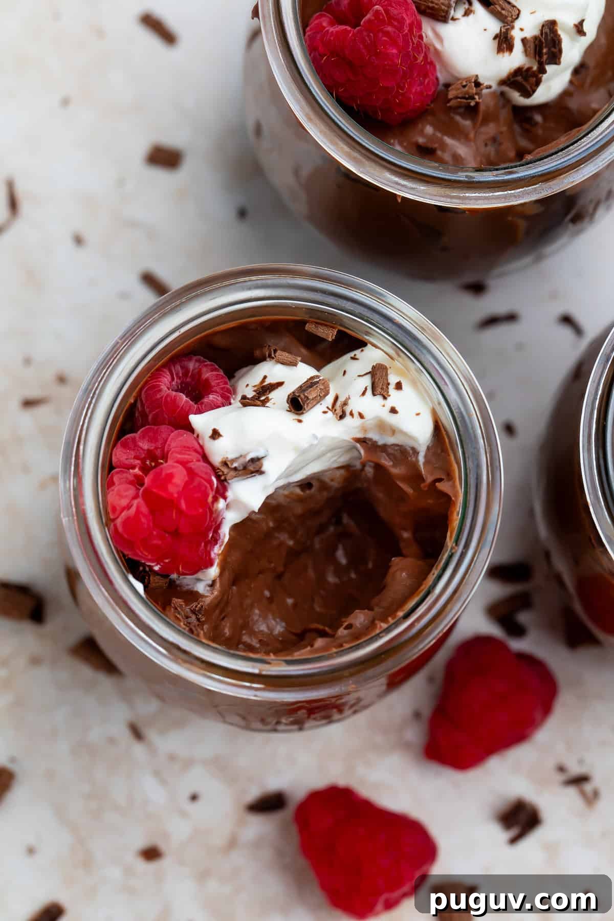 Overhead picture of two keto chocolate puddings topped with whipped cream, fresh raspberries and chocolate shavings.