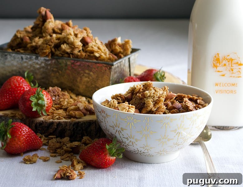 A bowl of maple almond granola sitting on a table next to milk and strawberries.