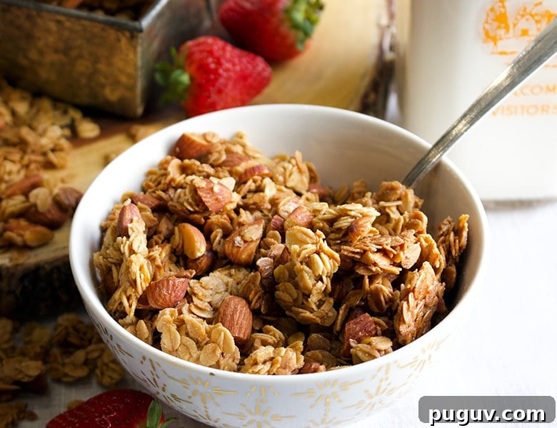 A bowl of maple almond granola sitting on a table next to milk and strawberries.