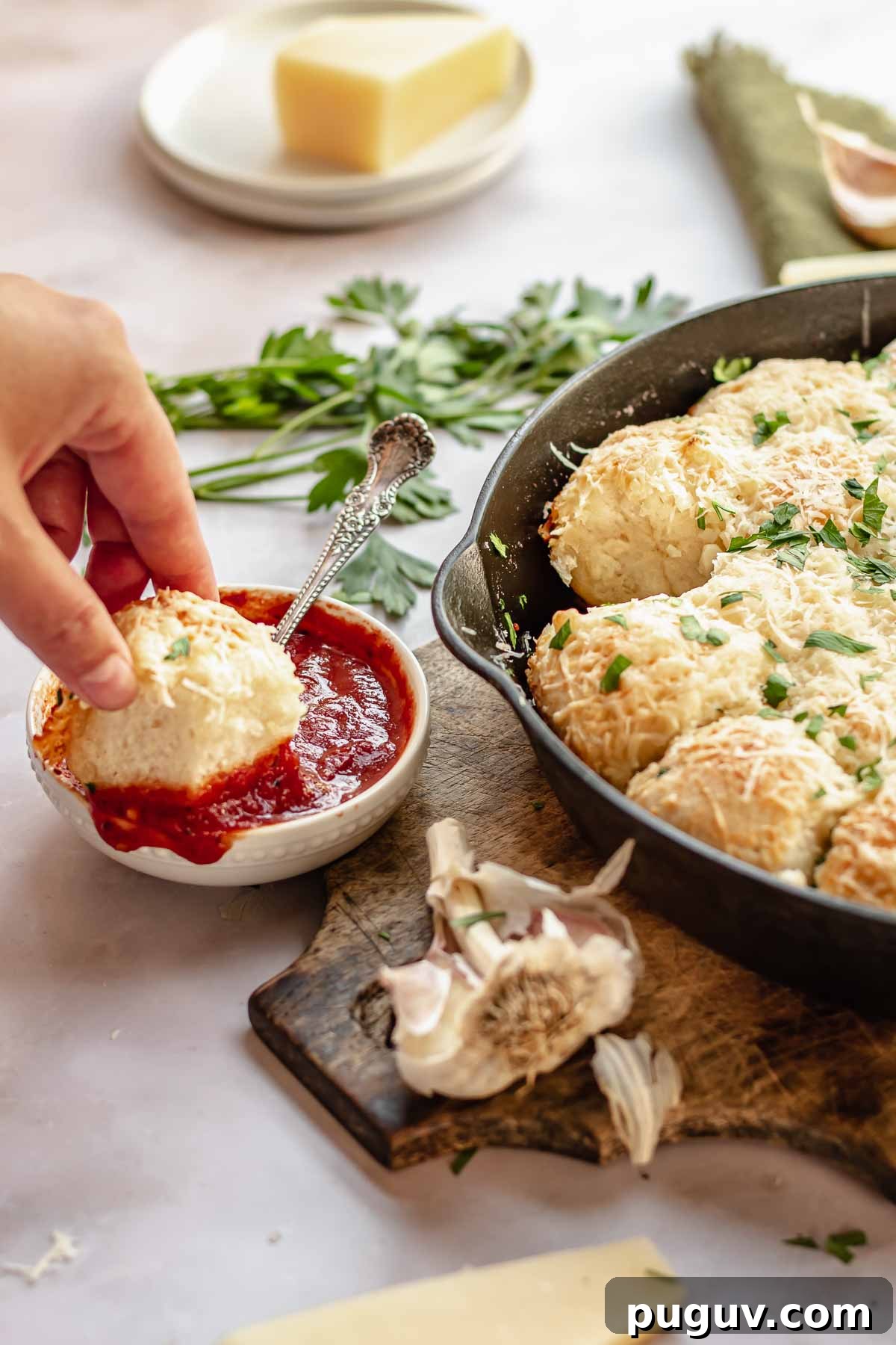A hand dunks a parmesan bread bite into bowl of pizza sauce.