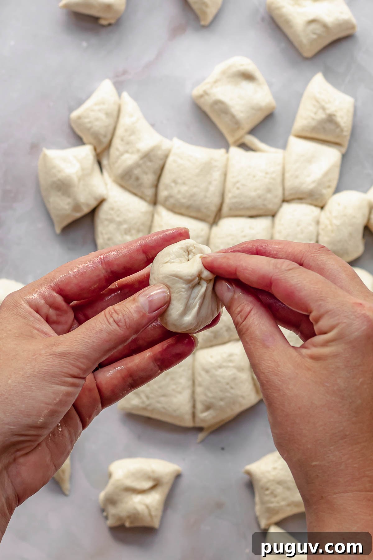 Hands pinch pizza dough into a round ball.